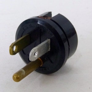 May include: A black electrical plug with two flat prongs and a round ground prong. The plug is made of black plastic and has a metal center.