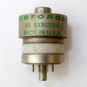May include: A silver-colored electronic component with a green label that reads "MOTOROLA 65 83382D02 MADE IN U.S.A."