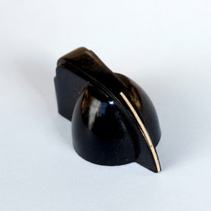 May include: A black, vintage-style knob with a glossy finish. The knob has a unique, curved shape with a light-colored accent stripe. It appears to be made of a hard, durable material, likely plastic or bakelite.