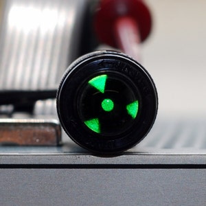 May include: Close-up of a black and green radiation symbol on a round, black object.