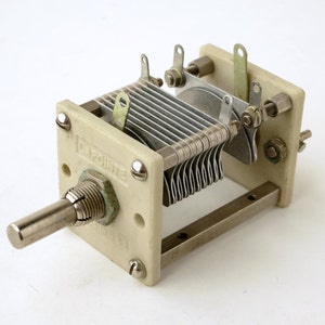 May include: A vintage variable capacitor with a cream-colored frame and silver metal plates. The capacitor has a long, silver shaft for adjustment and is labeled "LaPointe". The device is designed for use in electronic circuits.