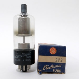 May include: A vintage General Electric 2V2 Electronic Tube in its original box. The tube is made in the USA and has a black base with nine pins. The box is blue with a white label that says "2V2 Electronic Tube".