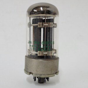 May include: A vintage vacuum tube with a clear glass enclosure and a metallic base. The tube contains internal components and has text that reads "JAN 6SN7GTB MADE IN USA". The top is a shiny, silver dome.