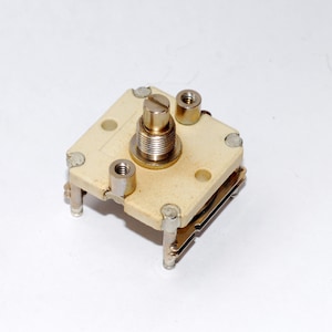 May include: A white ceramic variable capacitor with a silver metal tuning knob. The capacitor has four mounting holes and is designed for electronic circuits.