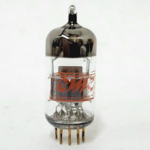 May include: A clear glass vacuum tube with a metallic silver top and gold pins at the base. The tube has orange lettering that reads "CMC". The internal components are visible through the glass.