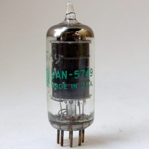 May include: A clear glass vacuum tube with a black metal base and a green label that reads "JAN-5749 MADE IN U.S.A."