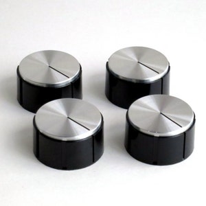May include: Four silver and black knobs with a single line across the top. The knobs are round and have a shiny finish.