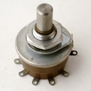 May include: A silver and brown potentiometer, a variable resistor used to control electrical current. It features a metal shaft, a mounting nut, and several connection terminals. The device is designed for electronic circuits.