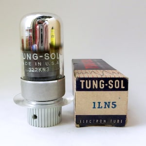 May include: A vintage Tung-Sol 1LN5 electron tube in its original box. The tube is made of glass and has a silver-colored metal base. The box is made of cardboard and has a brown and white color scheme. The text "Tung-Sol 1LN5 Electron Tube" is printed on the box.