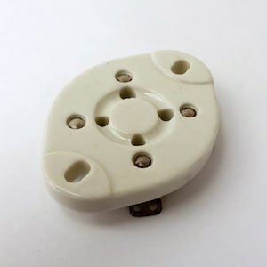 May include: A white ceramic electrical component with four metal contacts. The component has a circular center with a hole in the middle and a rounded oval shape.