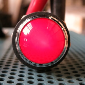 May include: A close-up of a red button with a silver rim. The button is mounted on a black surface.