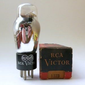 May include: A vintage RCA Victor vacuum tube with a clear glass bulb and a black base. The tube is next to a black and red RCA Victor box with the text "RCA Victor" and the number "12Z3".
