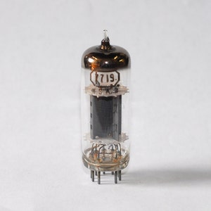 May include: A clear glass vacuum tube with a silver metal top and a black grid inside. The tube has a label that reads "719."
