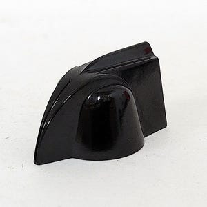 May include: A black plastic knob with a unique, angular design. The knob has a smooth, rounded top and a flat base.