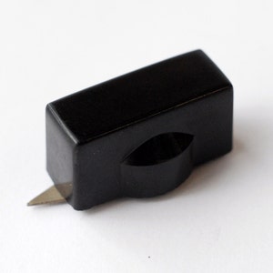 May include: A black plastic paper cutter with a sharp blade. The cutter has a rectangular shape with a rounded edge.