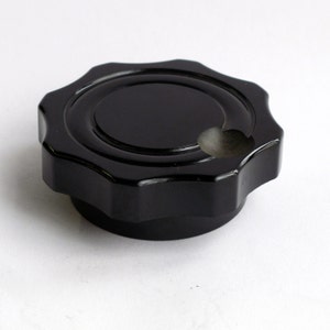 May include: A black plastic knob with a star-shaped design and a small hole in the center.
