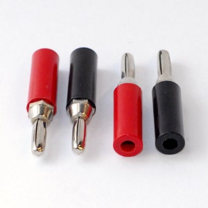 May include: Four electrical banana plugs consisting of two red and two black connectors. Two plugs feature exposed metal tips, while the other two show the cylindrical openings at the base. These components are designed for electronic cable connections.