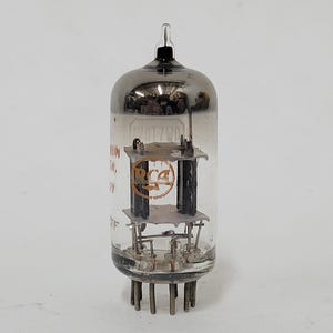 May include: Vintage RCA vacuum tube with a clear glass enclosure and a metallic top. The tube features internal components and a base with multiple pins. The RCA logo is visible on the internal structure. A classic electronic component.