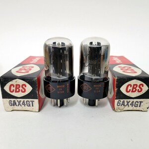 May include: Two vintage CBS 6AX4GT vacuum tubes with their original boxes. The tubes have a glass enclosure and black base with pins. The boxes are black and red with the CBS logo and tube model information. Made in the USA.