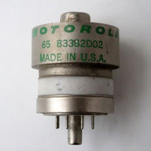 May include: A silver-colored electronic component with a green label that reads "MOTOROLA 65 83382D02 MADE IN U.S.A."