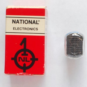 May include: A red box with the words "NATIONAL ELECTRONICS" and a black and white target with the number "1" and the letters "NL" inside. A small, clear, glass container with a black object inside.