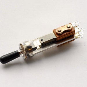 May include: A silver toggle switch with a black knob and a copper-colored contact plate. The switch has a chain-like design on the contact plate.