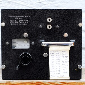 May include: A black precision condenser with a dial reading up to 1100. The condenser is labeled "General Radio Co." and "Cambridge Mass. U.S.A."  A white paper strip with the text "Corrections ABS. Dial Add 100 + 25 3/44 Perived Fro 300 -.54 worm 400 -.06 500 + 1.06 chert 606 -.07 and 700 -.27 Converte 800 -.10 900 -.19 INT 1000 -.13 t 1100 -.15 Aas, 722 5/1067" is attached to the condenser.