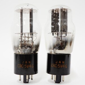 May include: Two vintage vacuum tubes with clear glass bulbs and black bases. The bases are labeled "JAN CRC-5V4-G". The internal components are visible through the glass. The tubes have multiple pins at the bottom.