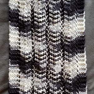 May include: A close-up of a knitted scarf with a black, white, and gray chevron pattern.