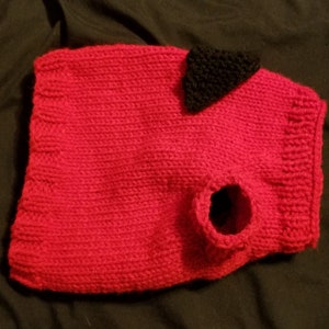 May include: A red knitted dog sweater with a black felt triangle on the back. The sweater has a hole for the dog's head and a hole for the leash.