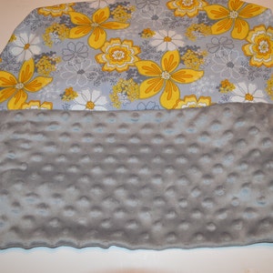 May include: A grey and yellow floral print fabric blanket with a soft, grey, textured backing.