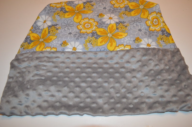 May include: A grey and yellow floral print fabric blanket with a soft, grey, textured backing.