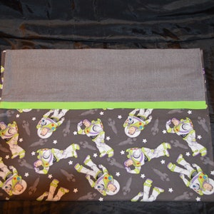Puede incluir: Una almohada de tela gris y verde con un patr&oacute;n de Buzz Lightyear de Toy Story sobre un fondo gris oscuro con estrellas blancas.