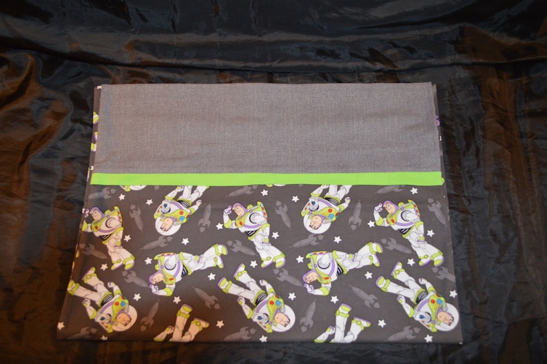 Puede incluir: Una almohada de tela gris y verde con un patr&oacute;n de Buzz Lightyear de Toy Story sobre un fondo gris oscuro con estrellas blancas.