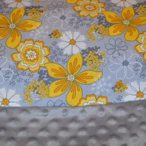 May include: A grey and white fabric with a yellow floral pattern. The fabric is soft and has a textured surface. The fabric is ideal for making blankets, cushions, and other home decor items.