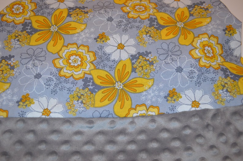 May include: A grey and white fabric with a yellow floral pattern. The fabric is soft and has a textured surface. The fabric is ideal for making blankets, cushions, and other home decor items.