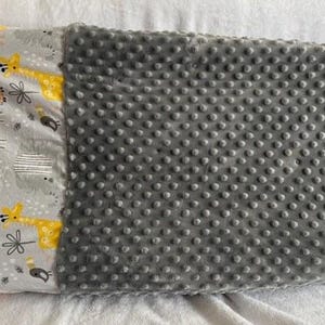 May include: A gray and yellow giraffe-themed pillowcase with a gray dimpled fabric on the other side. The pillowcase features a pattern of giraffes, monkeys, and other animal illustrations.