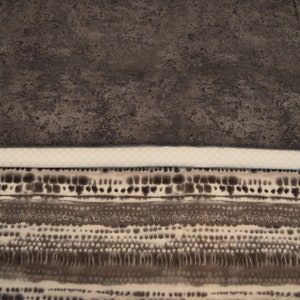May include: A close-up of a patterned fabric with a white background and brown and black abstract designs. The fabric has a subtle texture and a slightly distressed look.