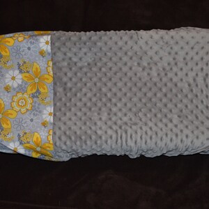 May include: A grey and white baby blanket with a yellow floral pattern on one side. The blanket is made of a soft, textured fabric.
