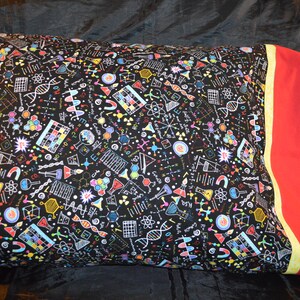 May include: A black pillowcase with a science-themed pattern featuring colorful illustrations of atoms, molecules, beakers, and other scientific symbols. The pillowcase has a red and yellow border.
