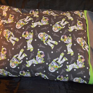 Puede incluir: Una funda de almohada gris con un patr&oacute;n repetido de Buzz Lightyear de Toy Story. La funda de almohada tiene un borde verde y gris.