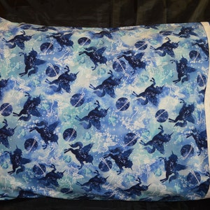 May include: A blue and white pillowcase with a pattern of flying unicorns and planets. The pillowcase has a blue border.