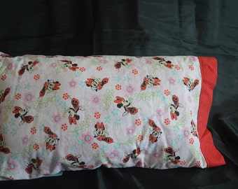 May include: A pink and white pillowcase with a red and black Minnie Mouse print. The pillowcase has a red border with white polka dots.