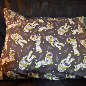 Puede incluir: Una funda de almohada gris con un patr&oacute;n repetido de Buzz Lightyear de Toy Story. El patr&oacute;n incluye a Buzz Lightyear en su traje de ranger espacial, estrellas y naves espaciales. La funda de almohada tiene un borde verde.