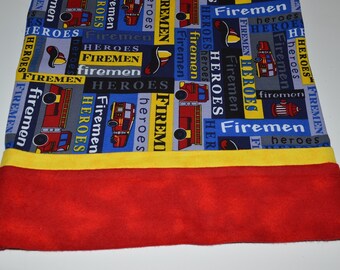 May include: A blue and black fabric with a repeating pattern of fire trucks, flames, and the words "Firemen" and "Heroes". The fabric has a yellow and red trim.