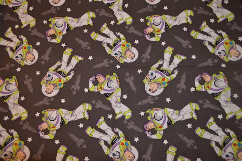 Puede incluir: Una tela gris con un patr&oacute;n repetido de un ranger espacial de dibujos animados en un traje espacial blanco y morado con una visera amarilla. El ranger espacial est&aacute; rodeado de estrellas blancas y cohetes grises.