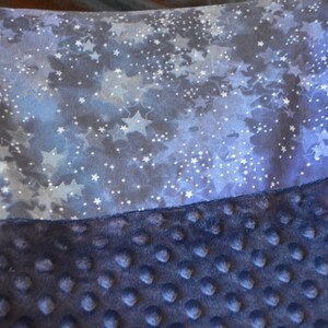 May include: A soft, blue and white baby blanket with a star pattern on one side and a textured, blue fabric on the other side.