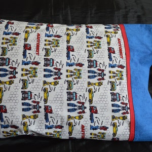 May include: A white pillowcase with a repeating pattern of yellow, blue, and red robots transforming into cars. The text "Autobot" is printed on the pillowcase. The pillowcase has a blue border with a red stripe.