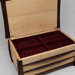 May include: A wooden jewelry box with a curved lid and three drawers. The box is made of maple and walnut wood and has a red velvet interior.