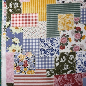 May include: A patchwork fabric with a variety of patterns and colors. The design includes squares of floral, gingham, striped, and solid fabrics in shades of blue, red, yellow, green, and pink. The fabric is likely for quilting or crafting.